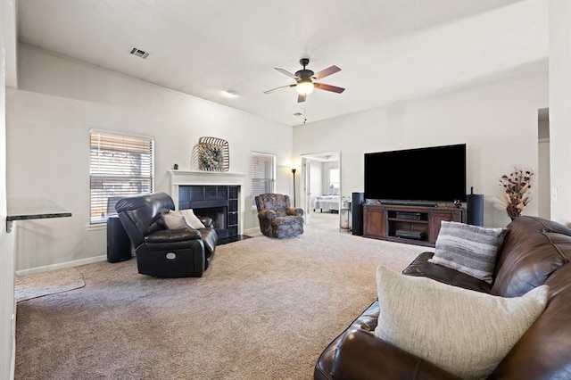 living room with a tile fireplace, carpet, and ceiling fan