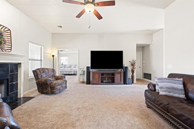 living room with ceiling fan, a tiled fireplace, and dark carpet