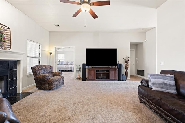 living room with ceiling fan, a tiled fireplace, and dark colored carpet