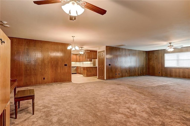 unfurnished living room with ceiling fan with notable chandelier, light colored carpet, and wood walls