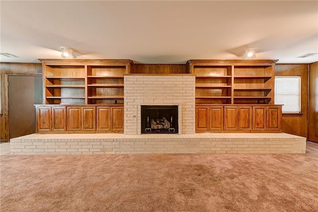 unfurnished living room with wood walls, light colored carpet, and a brick fireplace