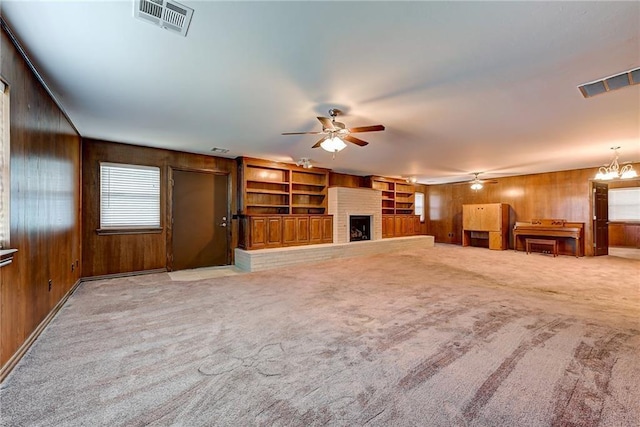 unfurnished living room featuring a brick fireplace, carpet floors, built in features, ceiling fan, and wood walls