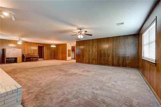 unfurnished living room with ceiling fan with notable chandelier, wooden walls, and carpet