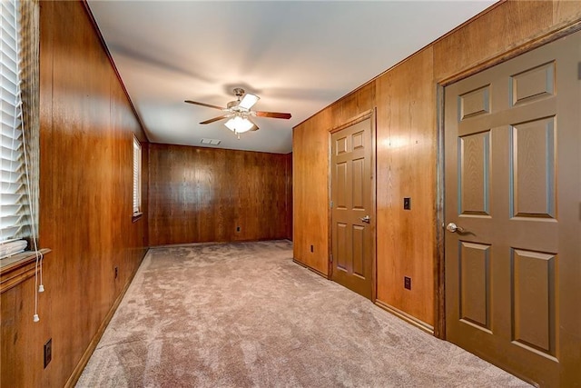 unfurnished room with ceiling fan, light colored carpet, and wooden walls