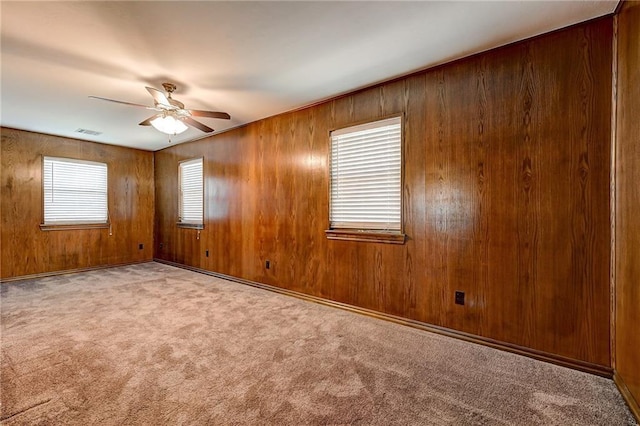 unfurnished room featuring light carpet, wood walls, and ceiling fan