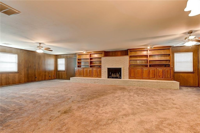 unfurnished living room featuring a fireplace, built in features, light carpet, and ceiling fan