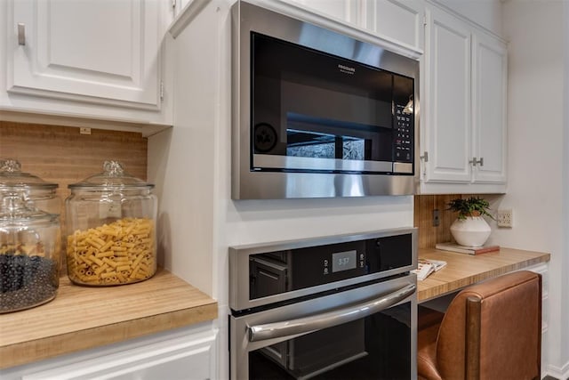 kitchen featuring tasteful backsplash, built in desk, stainless steel oven, and white cabinets