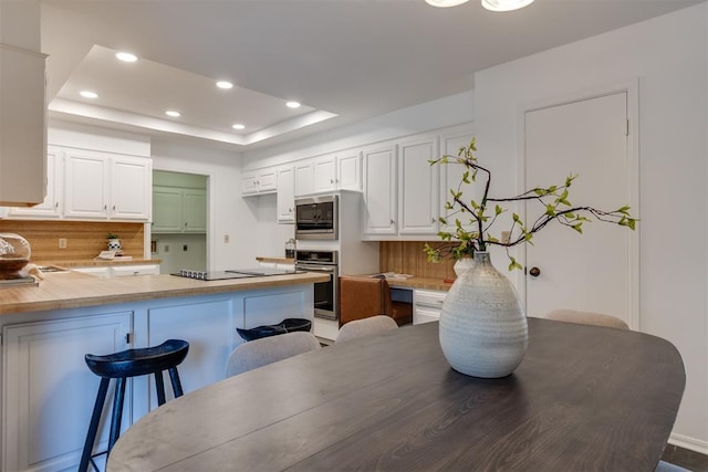 kitchen featuring white cabinetry, appliances with stainless steel finishes, a tray ceiling, and kitchen peninsula