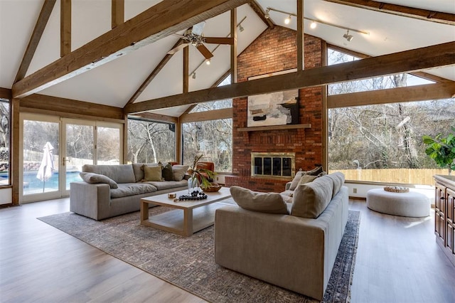 living room with wood-type flooring, a brick fireplace, track lighting, beamed ceiling, and ceiling fan