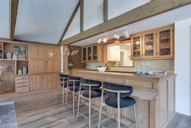 kitchen featuring sink, light hardwood / wood-style floors, lofted ceiling with beams, and a breakfast bar area