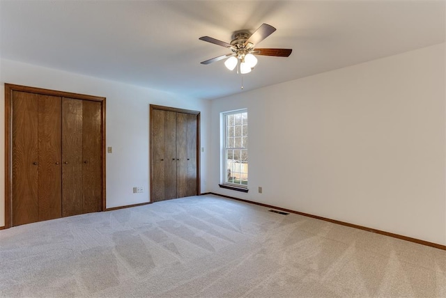 unfurnished bedroom with two closets, light colored carpet, and ceiling fan