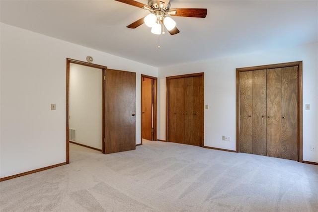 unfurnished bedroom featuring ceiling fan, light colored carpet, and two closets