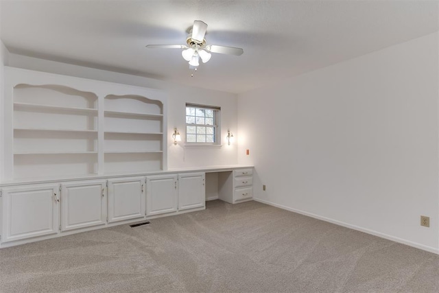 unfurnished room with ceiling fan, built in desk, and light carpet