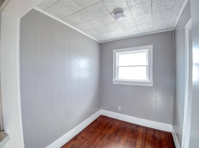 unfurnished room with crown molding, wood walls, and dark wood-type flooring