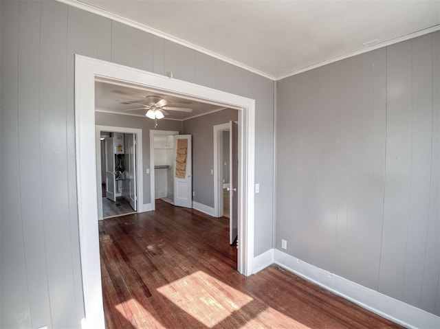 empty room with wood walls, dark wood-type flooring, ceiling fan, and ornamental molding