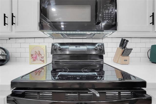 interior details featuring white cabinetry, decorative backsplash, and black appliances