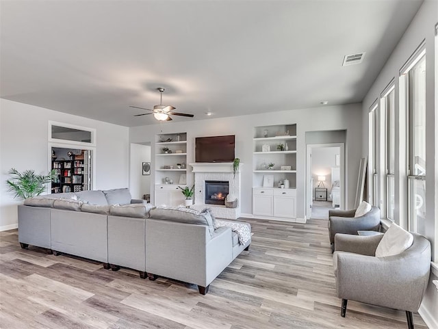 living room featuring built in features, light hardwood / wood-style floors, and ceiling fan