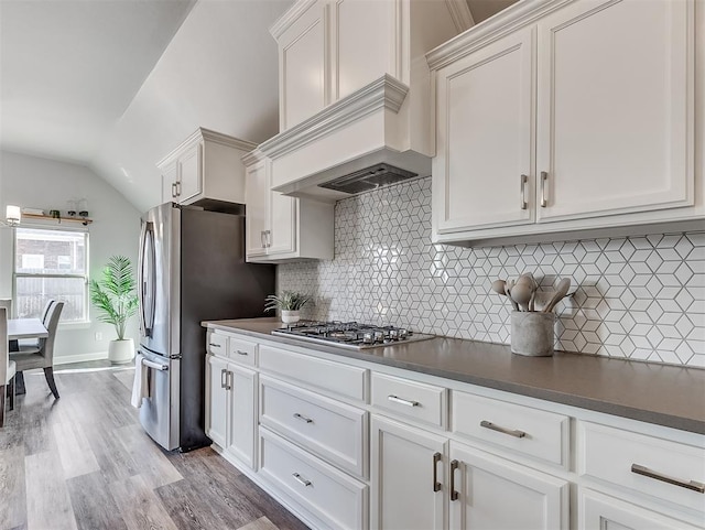 kitchen featuring lofted ceiling, stainless steel appliances, light hardwood / wood-style floors, decorative backsplash, and white cabinets