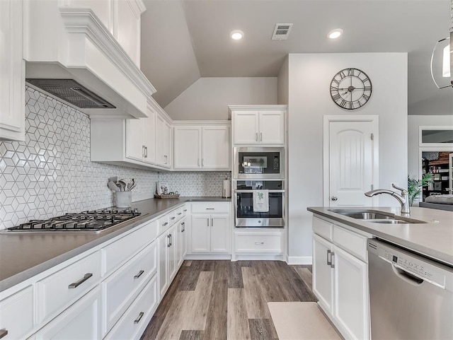 kitchen featuring sink, white cabinets, decorative backsplash, stainless steel appliances, and custom range hood