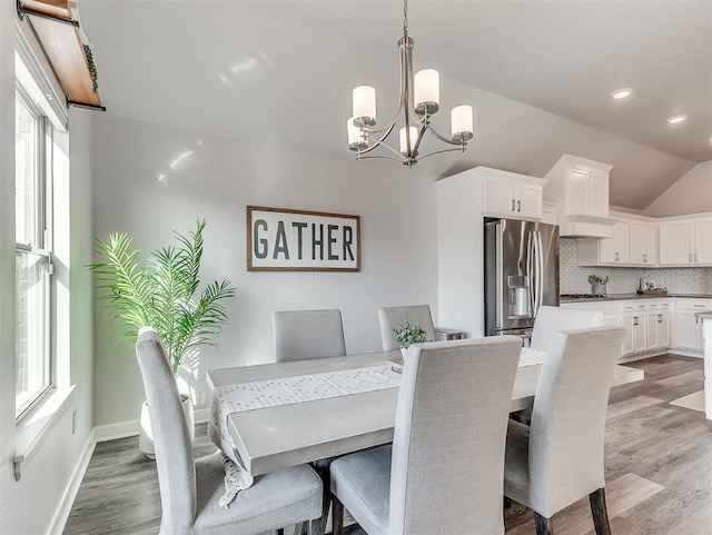 dining room with a wealth of natural light, vaulted ceiling, a chandelier, and light wood-type flooring