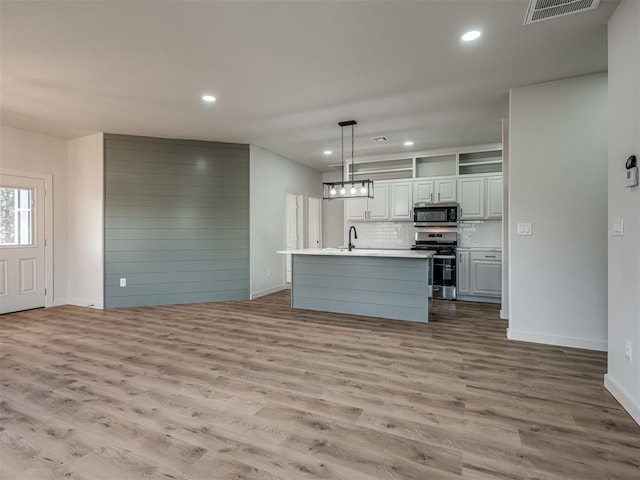 kitchen with decorative light fixtures, light hardwood / wood-style flooring, an island with sink, and appliances with stainless steel finishes