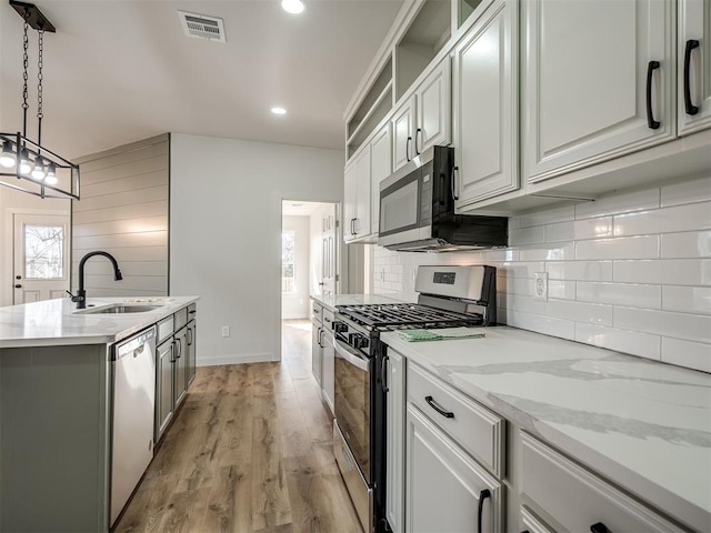 kitchen featuring sink, stainless steel appliances, light hardwood / wood-style floors, white cabinets, and decorative light fixtures