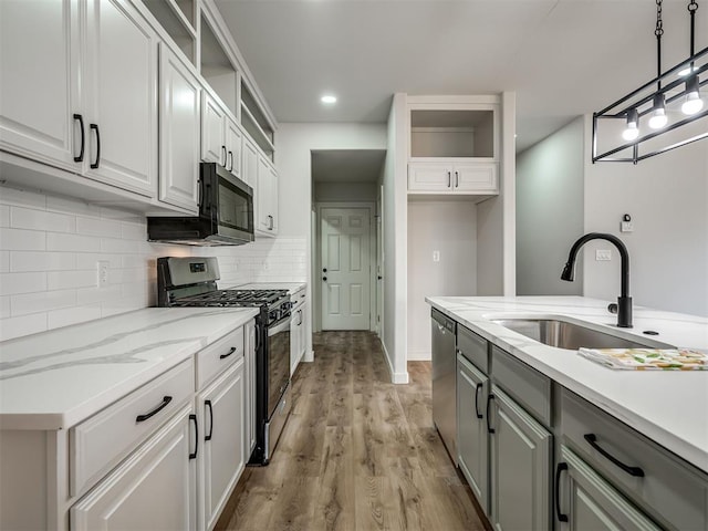 kitchen featuring light stone counters, decorative light fixtures, stainless steel appliances, white cabinetry, and a sink