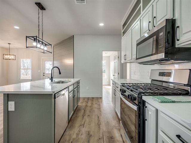 kitchen with appliances with stainless steel finishes, white cabinetry, backsplash, hanging light fixtures, and a kitchen island with sink