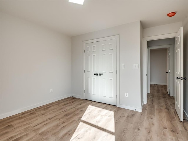 unfurnished bedroom with baseboards, a closet, and light wood-style floors