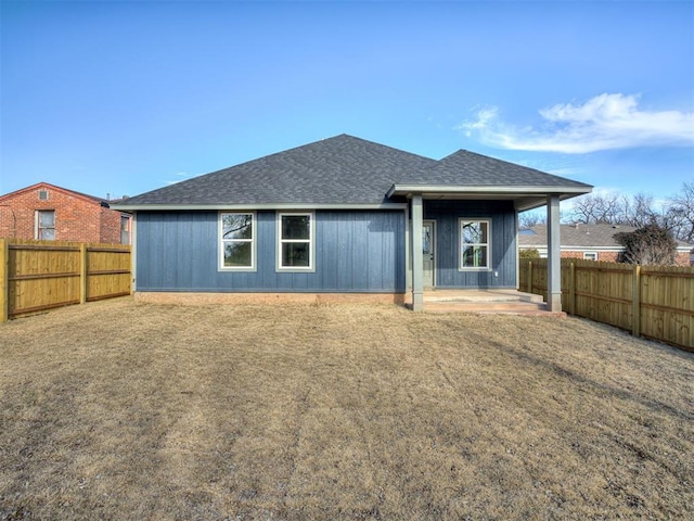 rear view of house featuring roof with shingles, a patio area, a fenced backyard, and a lawn