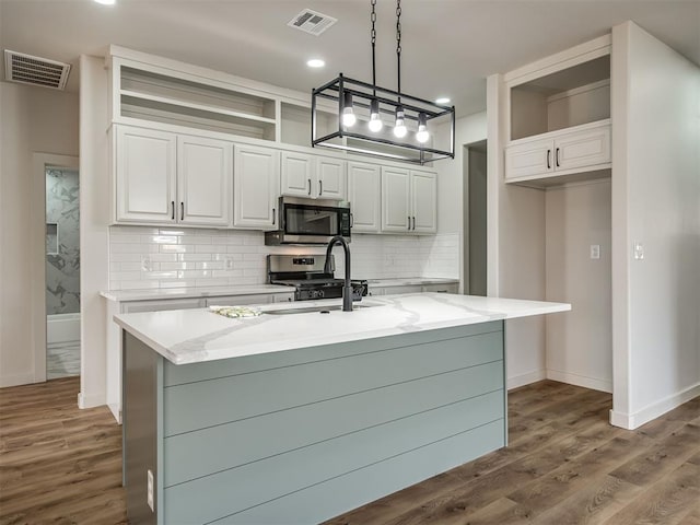 kitchen with stainless steel appliances, a kitchen island with sink, hanging light fixtures, and white cabinets