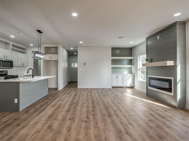 kitchen featuring a glass covered fireplace, open floor plan, decorative light fixtures, stainless steel appliances, and light countertops