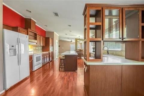 kitchen with a center island, white appliances, hardwood / wood-style flooring, decorative backsplash, and a kitchen breakfast bar