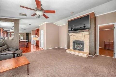 carpeted living room with ceiling fan, a stone fireplace, and vaulted ceiling