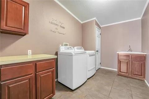 clothes washing area with washing machine and dryer, ornamental molding, cabinets, and sink