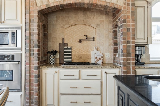 kitchen featuring stone counters, tasteful backsplash, appliances with stainless steel finishes, and brick wall