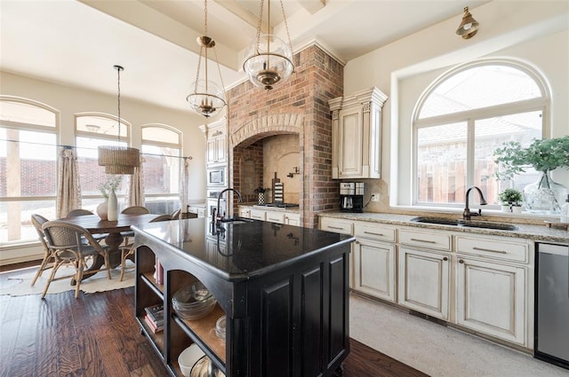 kitchen featuring decorative light fixtures, an island with sink, sink, backsplash, and cream cabinets