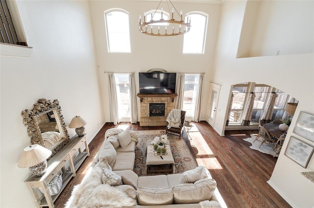 living room with a chandelier, a towering ceiling, a stone fireplace, and dark hardwood / wood-style flooring