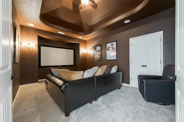 home theater with a raised ceiling, light carpet, and ceiling fan