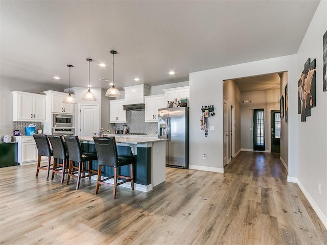 kitchen featuring appliances with stainless steel finishes, pendant lighting, tasteful backsplash, white cabinetry, and a center island with sink