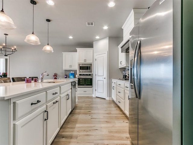 kitchen with appliances with stainless steel finishes, an island with sink, pendant lighting, decorative backsplash, and white cabinets