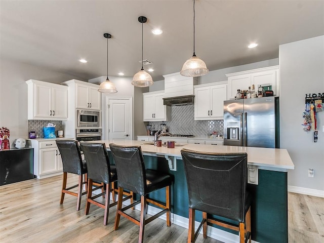 kitchen featuring white cabinetry, hanging light fixtures, stainless steel appliances, tasteful backsplash, and an island with sink