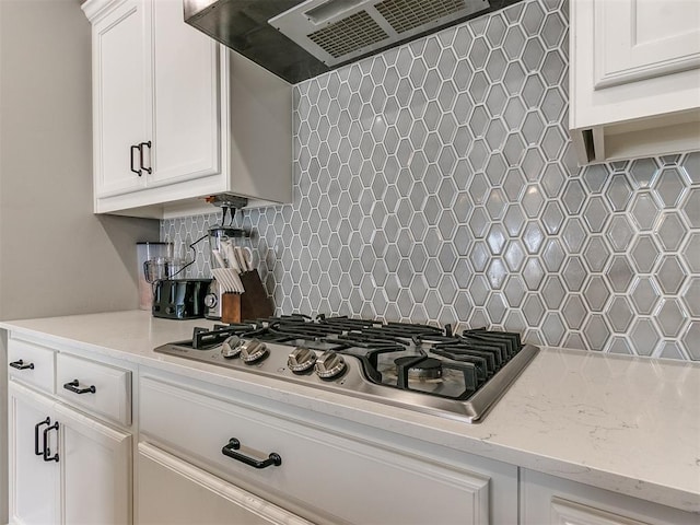 kitchen with wall chimney range hood, backsplash, light stone countertops, white cabinets, and stainless steel gas stovetop