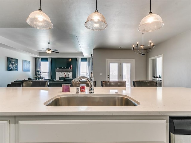 kitchen with sink, ceiling fan, hanging light fixtures, light stone countertops, and french doors