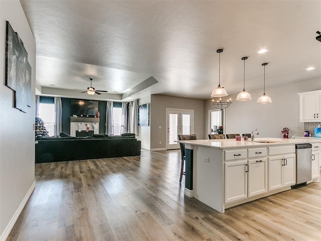 kitchen with sink, a kitchen island with sink, hanging light fixtures, white cabinets, and stainless steel dishwasher