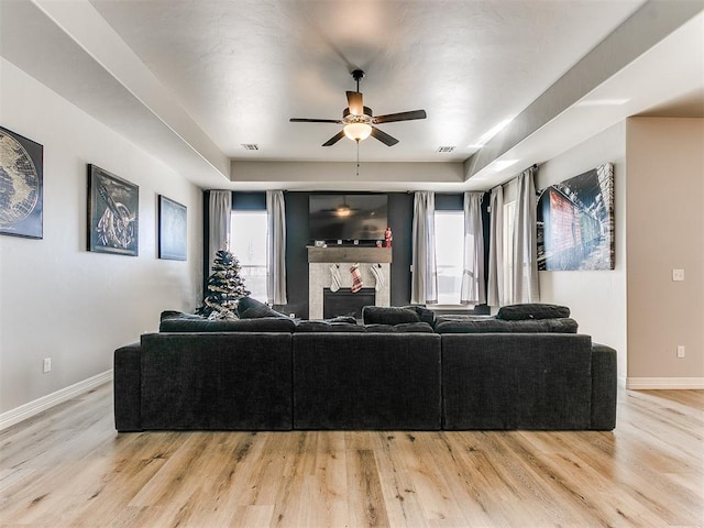 living room with light hardwood / wood-style flooring, a tray ceiling, a fireplace, and ceiling fan