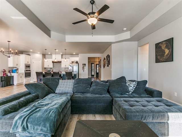 living room featuring ceiling fan with notable chandelier and light hardwood / wood-style floors