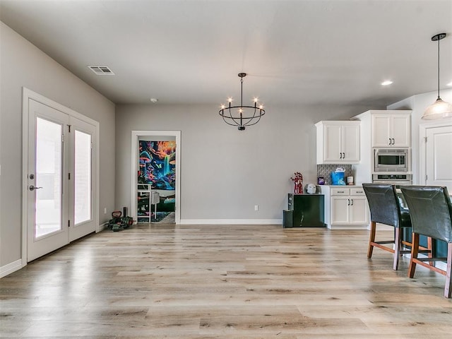 kitchen featuring stainless steel microwave, white cabinets, backsplash, and decorative light fixtures