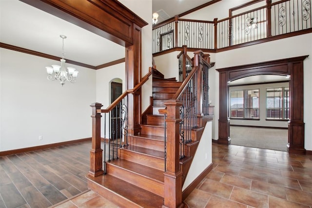 stairs featuring ornamental molding, wood-type flooring, a towering ceiling, and a notable chandelier