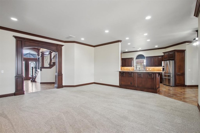 unfurnished living room featuring ceiling fan, ornamental molding, sink, and dark carpet